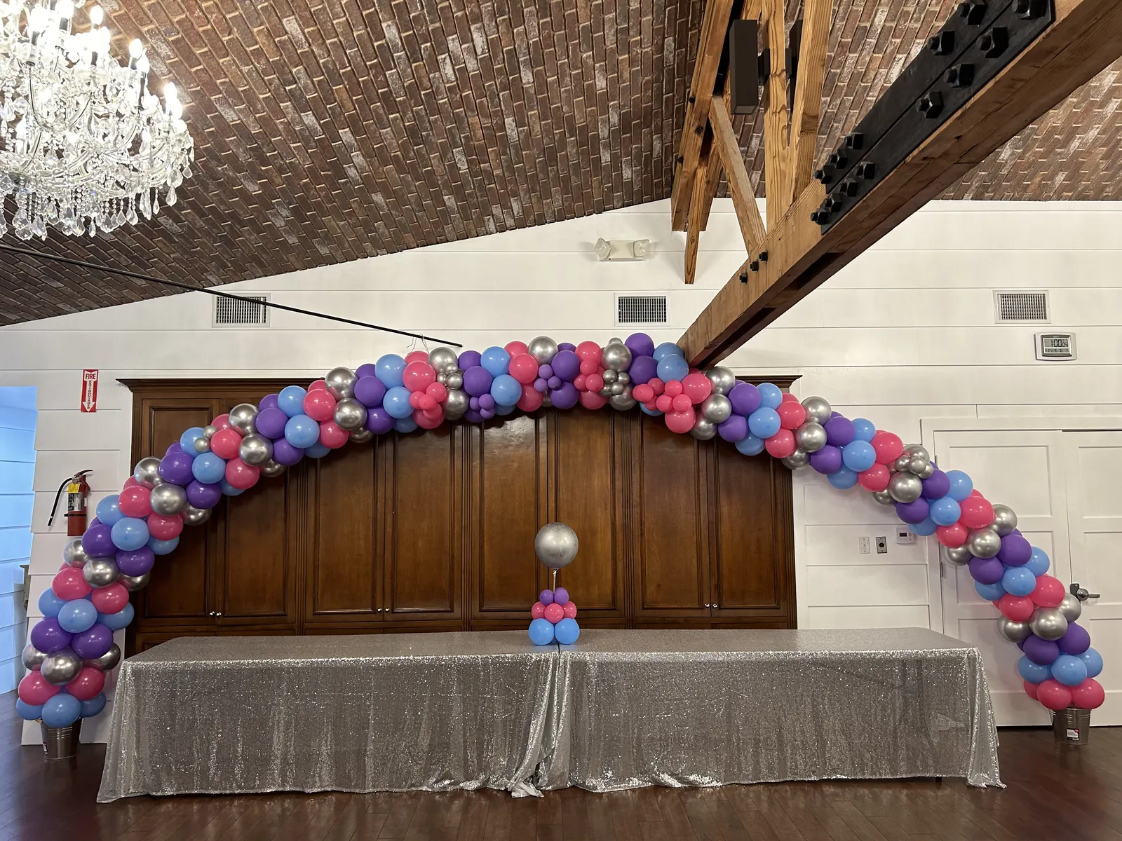 20 foot pink, purple and silver balloon arch over a head table in a Los Angeles event hall