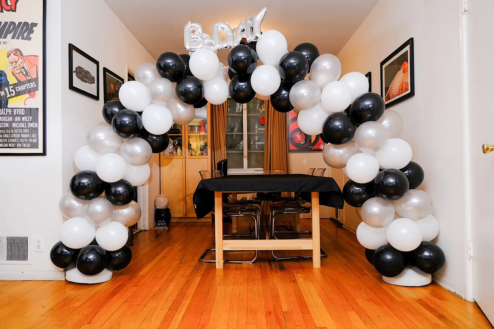 Black, white and silver balloon arch with a B-Day balloon in a dining room