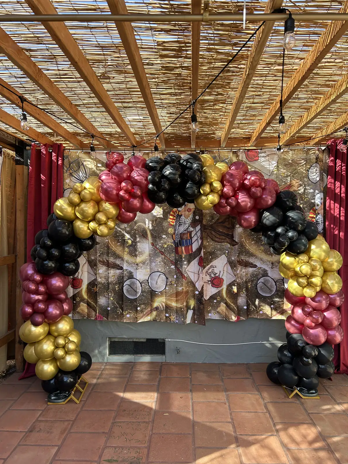 Balloon arch in burgundy, gold and black for a wizard-themed party on a Los Angeles patio