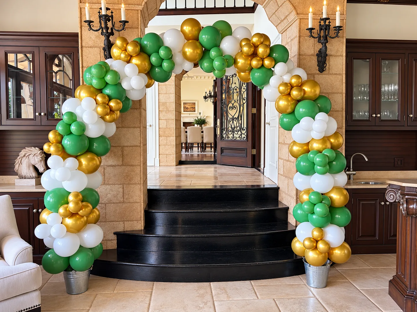 Green, chrome gold and white organic balloon arch over a stone entryway and black stairs in a Bel Air home
