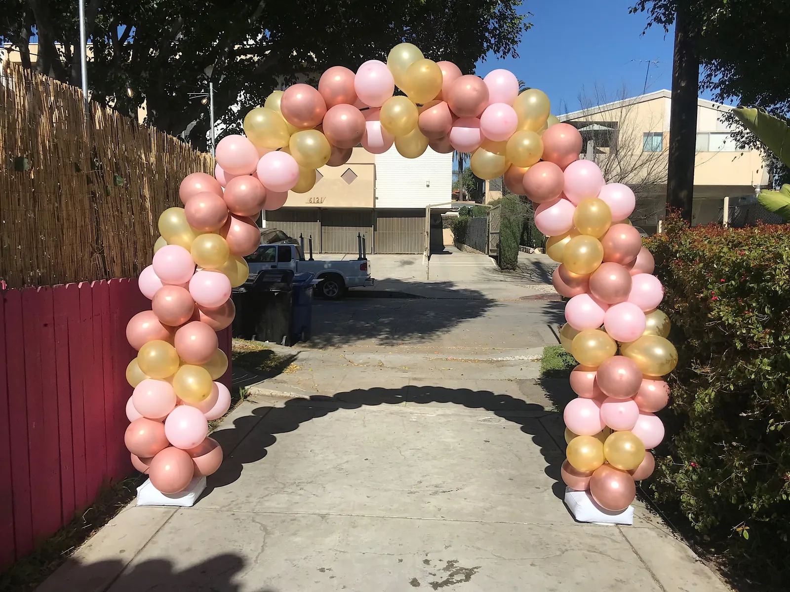 Pink and gold balloon arch over a driveway