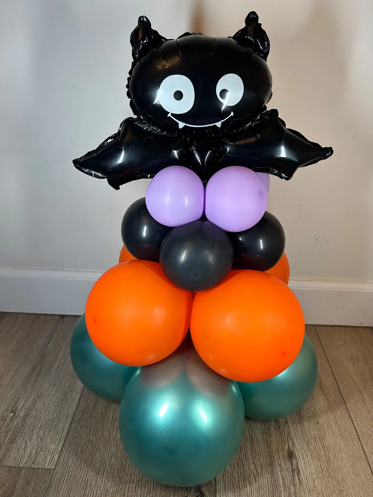 Halloween balloon centerpiece with a bat foil balloon over orange, black and teal balloons