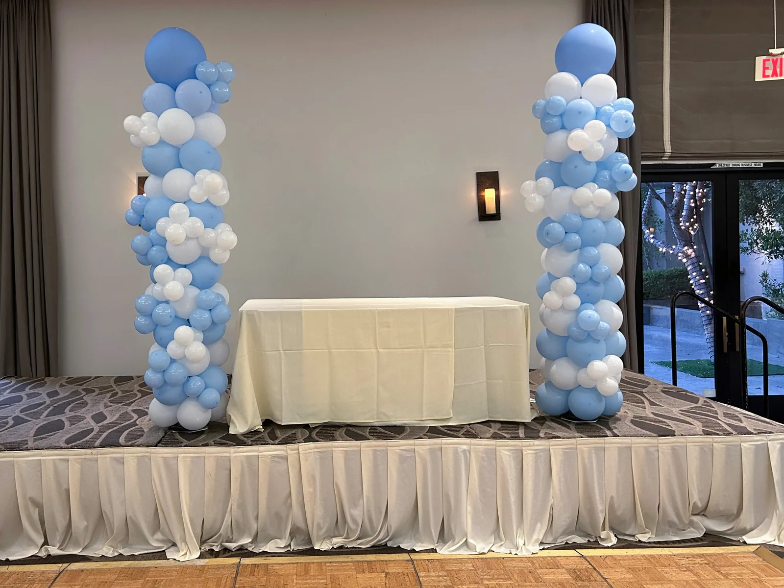 Pair of light blue and white organic balloon columns on either side of a head table on an event hall stage