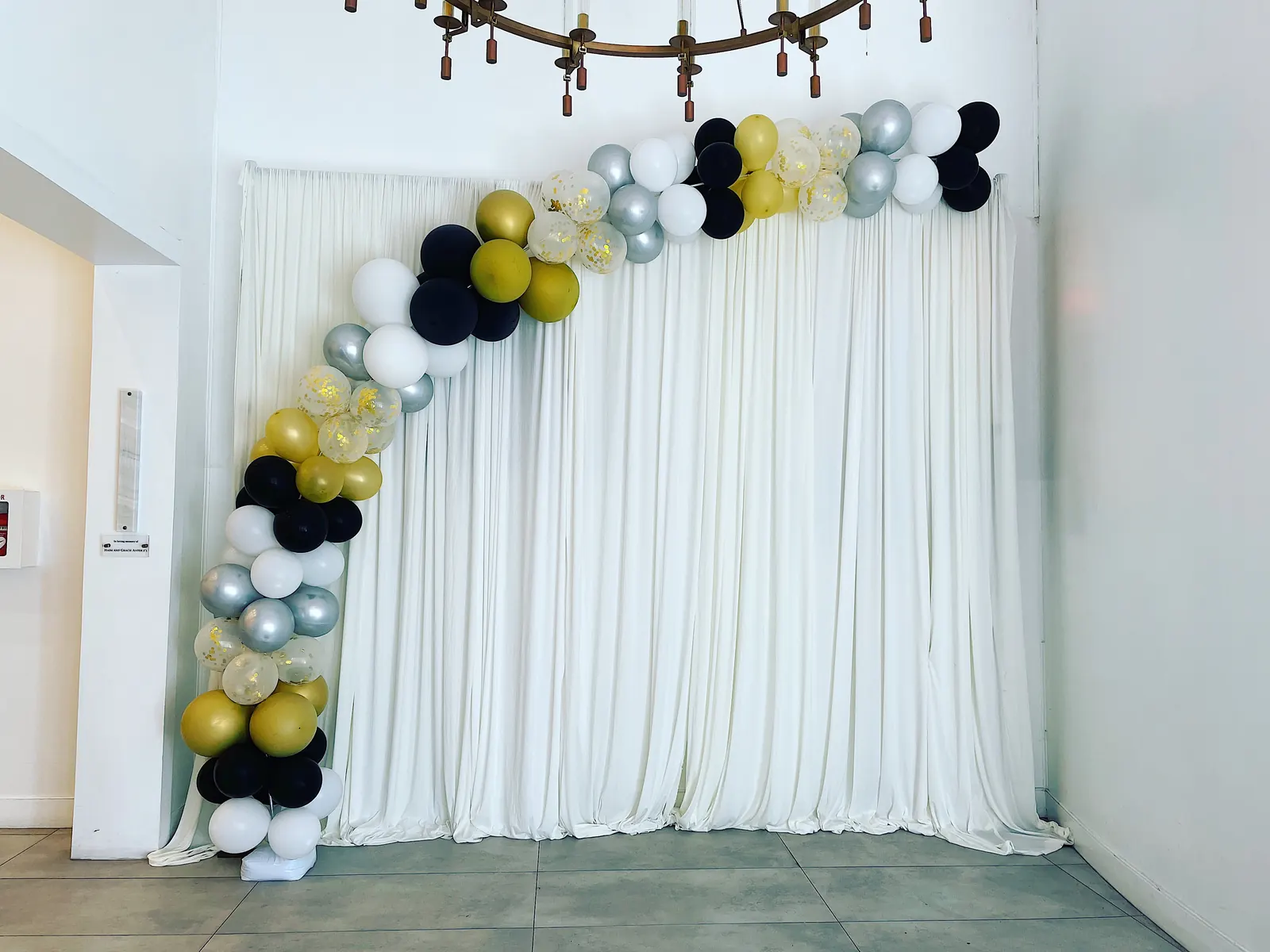 Black, gold, silver and white balloon garland over a white drape backdrop in Los Angeles
