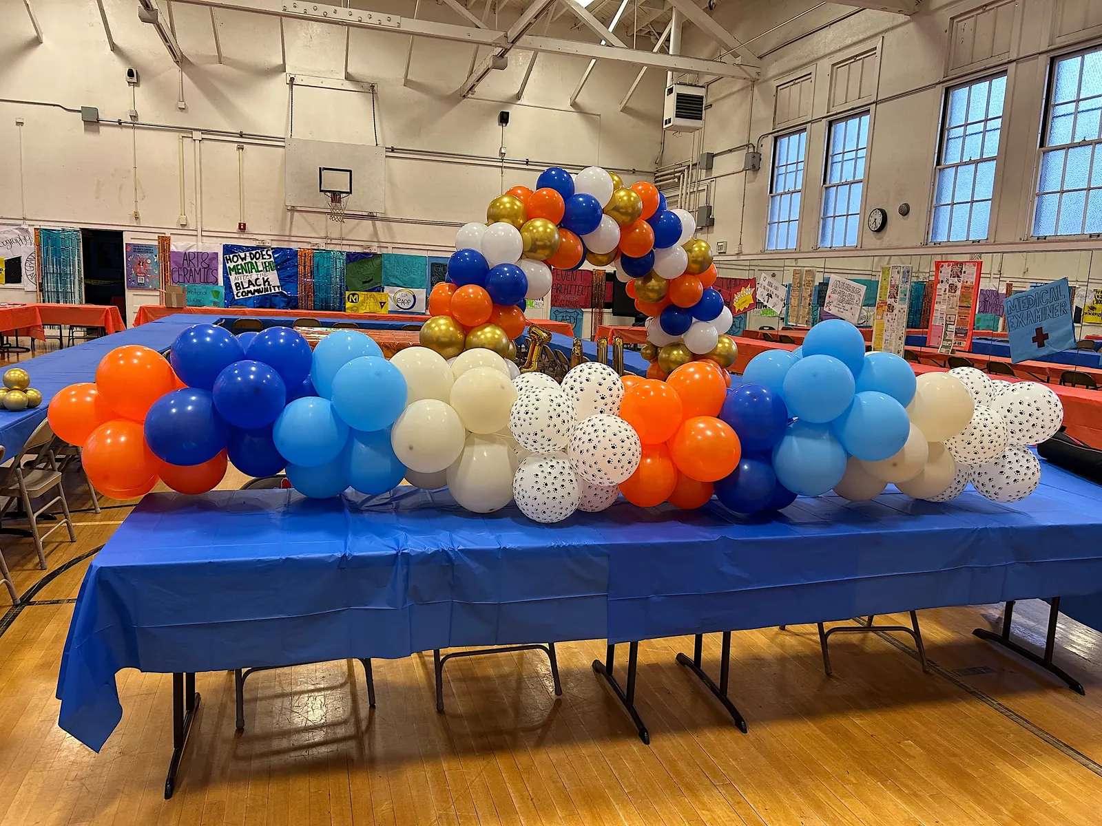 Orange, blue and polka dot balloon garland on a long table in a school gym
