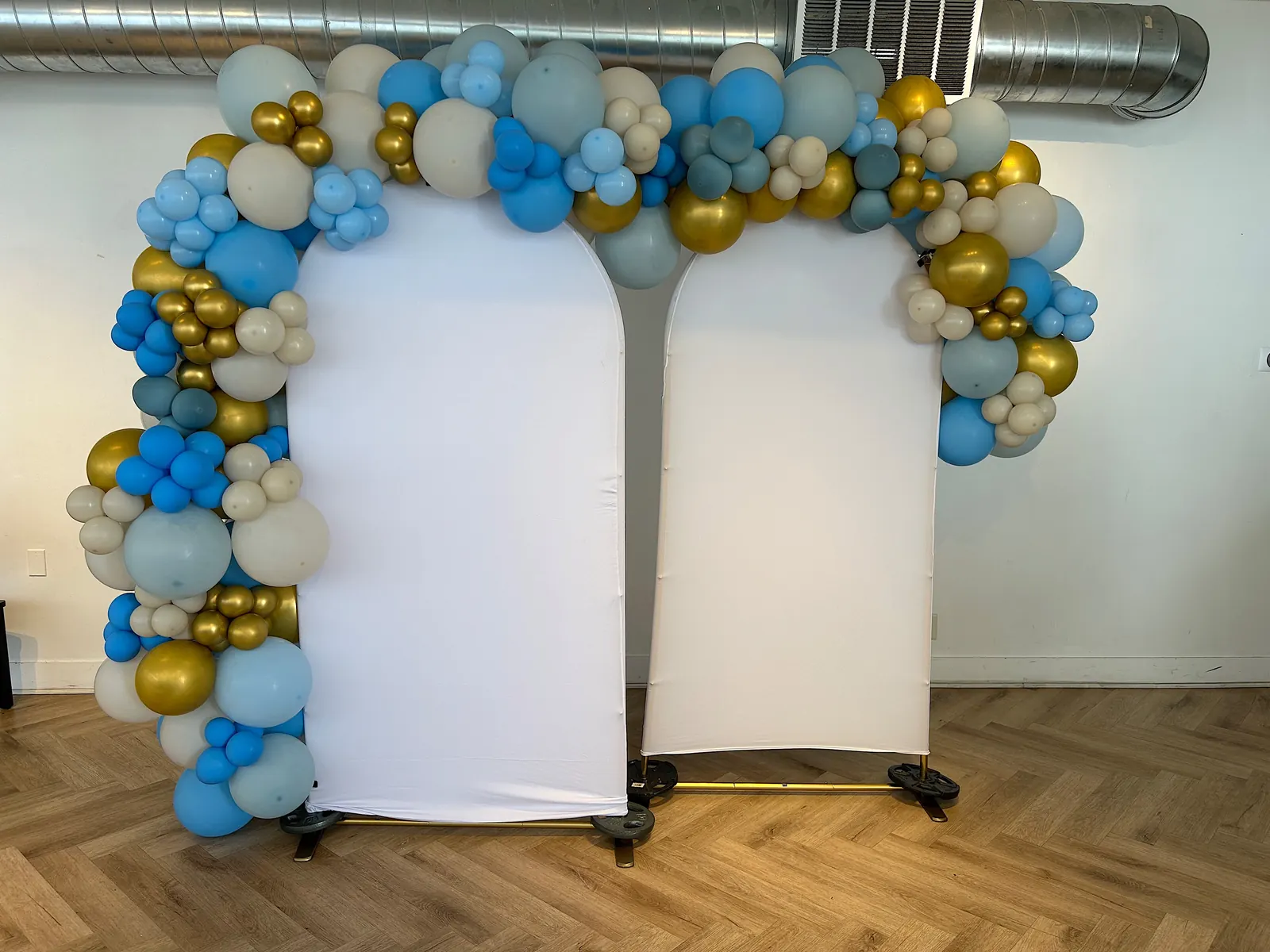 Two arched Chiara backdrops joined by a blue, sand and gold organic garland