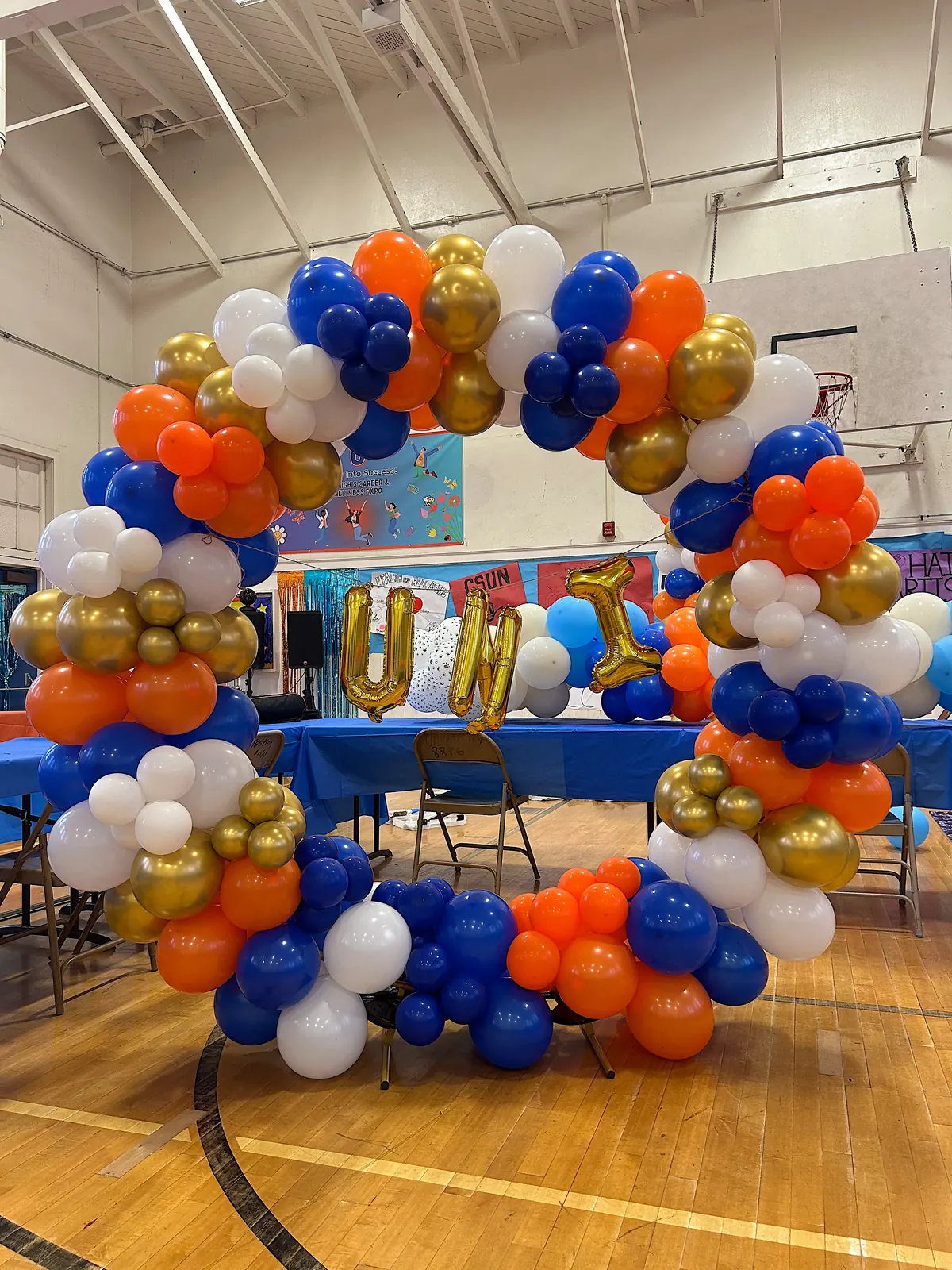 Blue, orange, gold and white circular balloon arch in a school gym