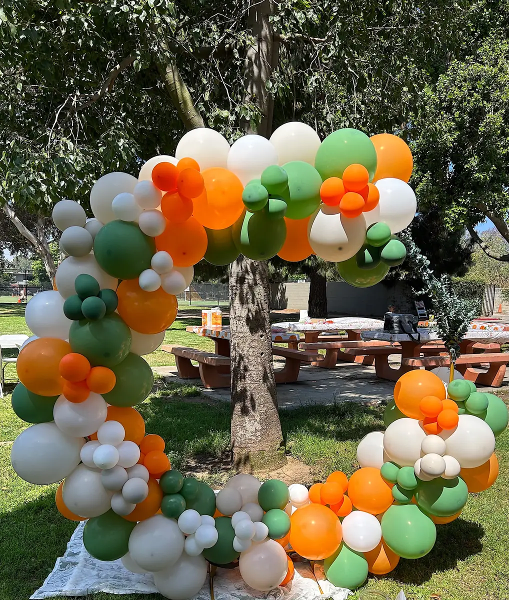 Circular balloon arch in orange, sage green and white in a park