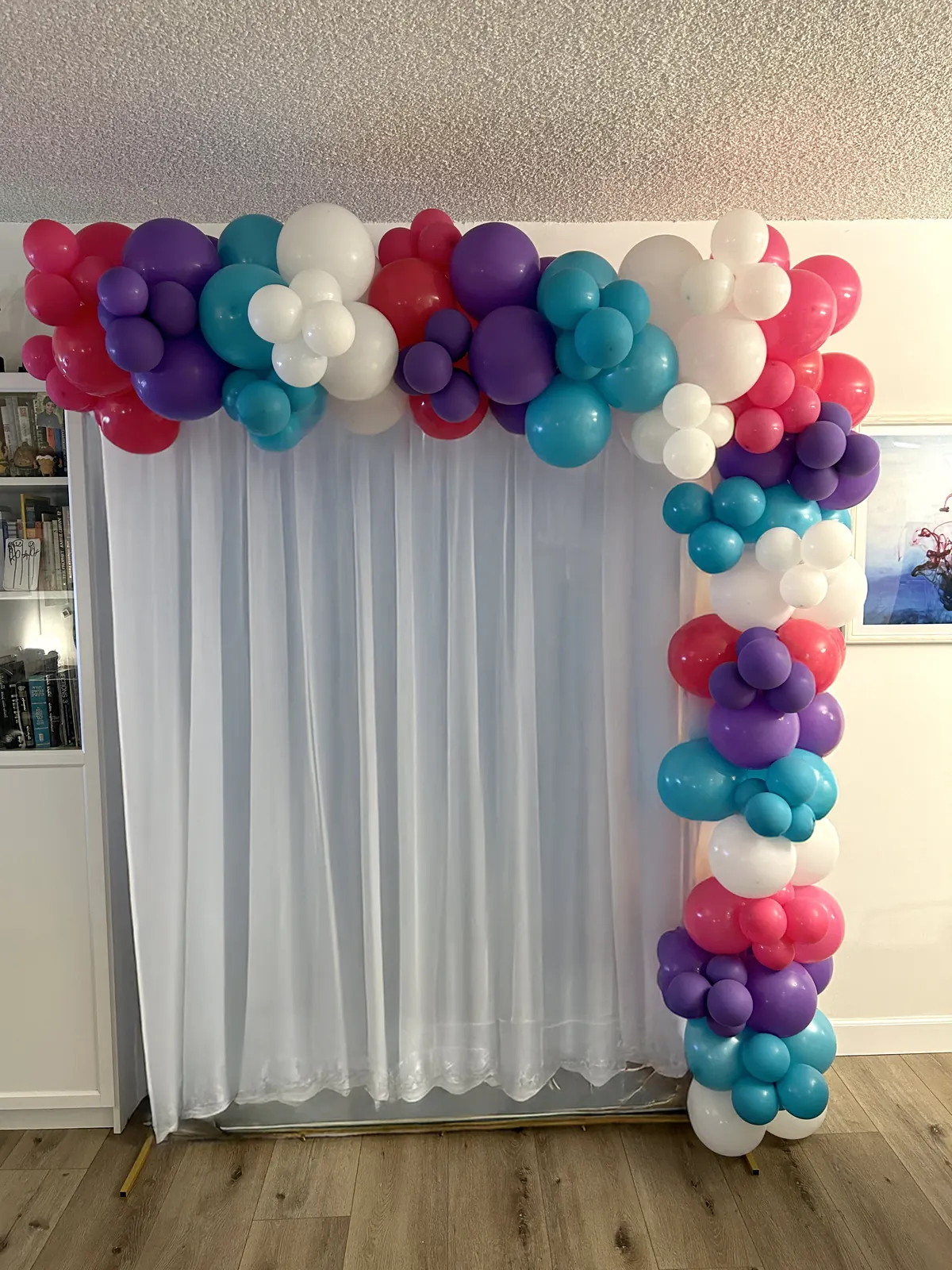 Rectangular photo backdrop in Los Angeles with a pink, purple, teal and white garland over a sheer curtain