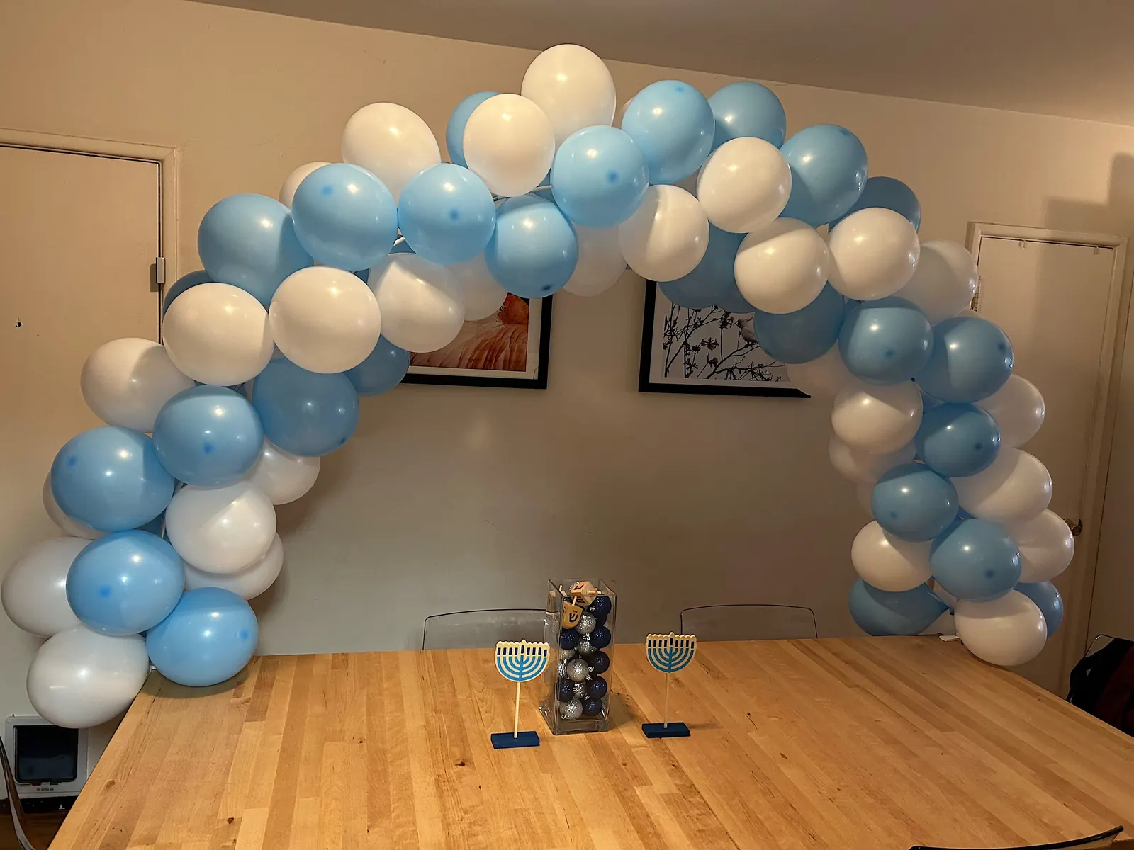 Light blue and white table balloon arch over a Hanukkah table with menorahs