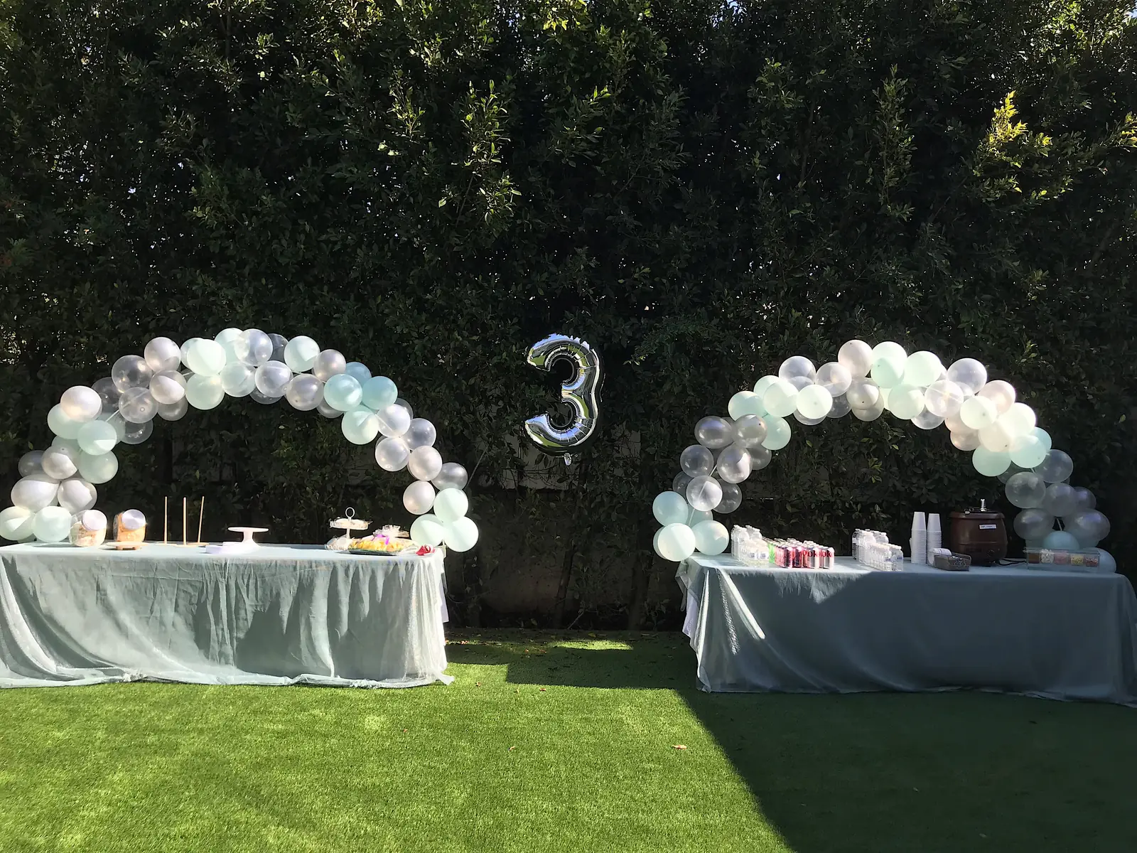 Two pearl white table balloon arches for a third birthday in a Los Angeles backyard