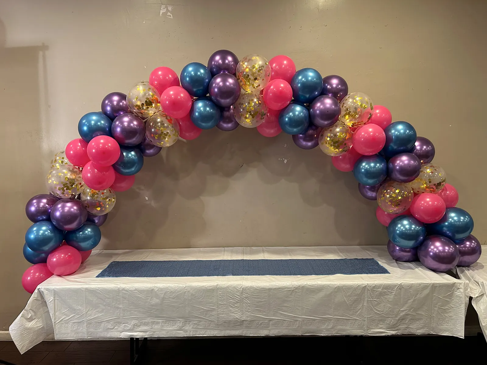 Table balloon arch in purple, pink, teal and gold confetti over a serving table